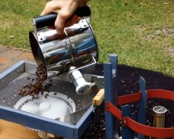 A screenshot of Larry Cotton's Wobble Disk Home Coffee Roaster in action. The handle encompasses the roasting chamber, which tips over to drop the coffee in a metal mesh bed.