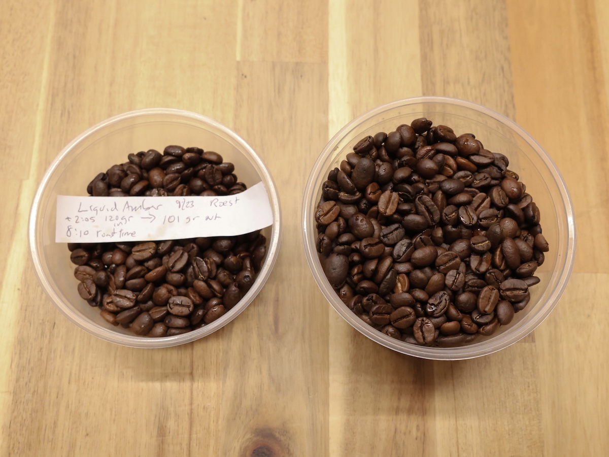 A shot of two deli tubs full of Sweet Maria's Liquid Amber Blend, roasted dark. Inside the left tub, there is a slip of paper with handwriting indicating that it is Liquid Amber.